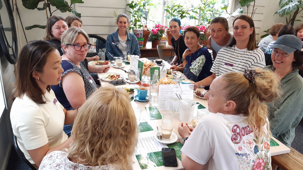 Group of women sitting around a lunch table in a cafe chatting