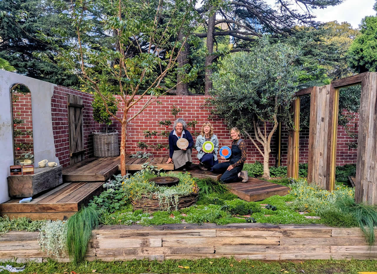 Three women crouching in a display garden holding their awards.