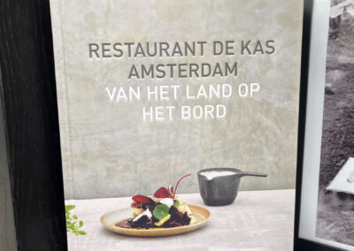 Photo of a book sitting on a shelf in a window. It is about Restaurant De Kas.